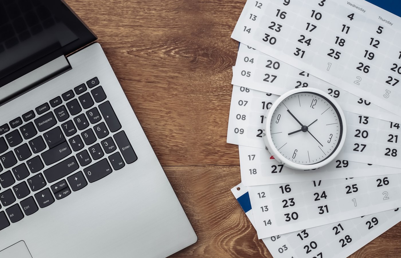 overhead view of a laptop, pages from a calendar, and a clock