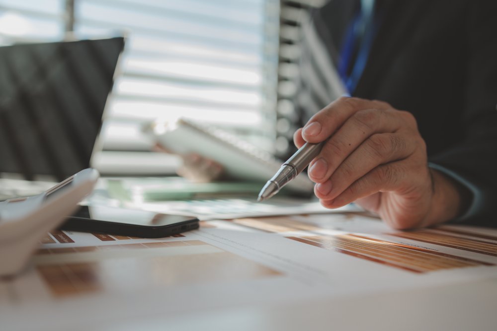 person holding pen and working with computer in background